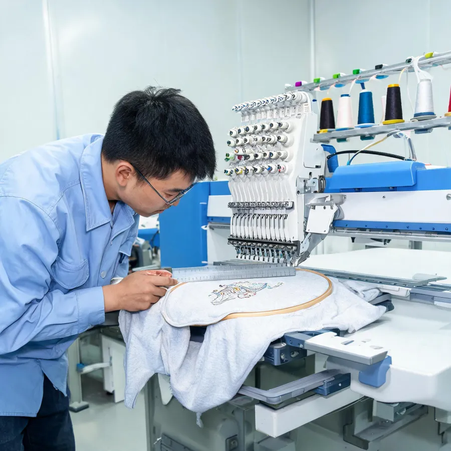 Embroidery operator reviewing a hoop, needle field, and production sample